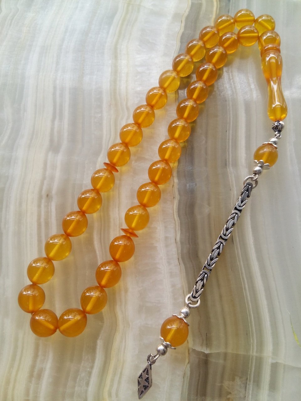 Özel İşçilikli Atölye Yapımı 925 Ayar Gümüş Püsküllü Ateş Kehribar Tesbih.Ürün Piyasanın en iyi Hammaddesinden Yapılmış Olup Canlı Rengiyle, Yumuşak Dokusu ve Kusursuz İşçiligiyle Tesbih Severlerin Beğenisine Sunulmuştur.