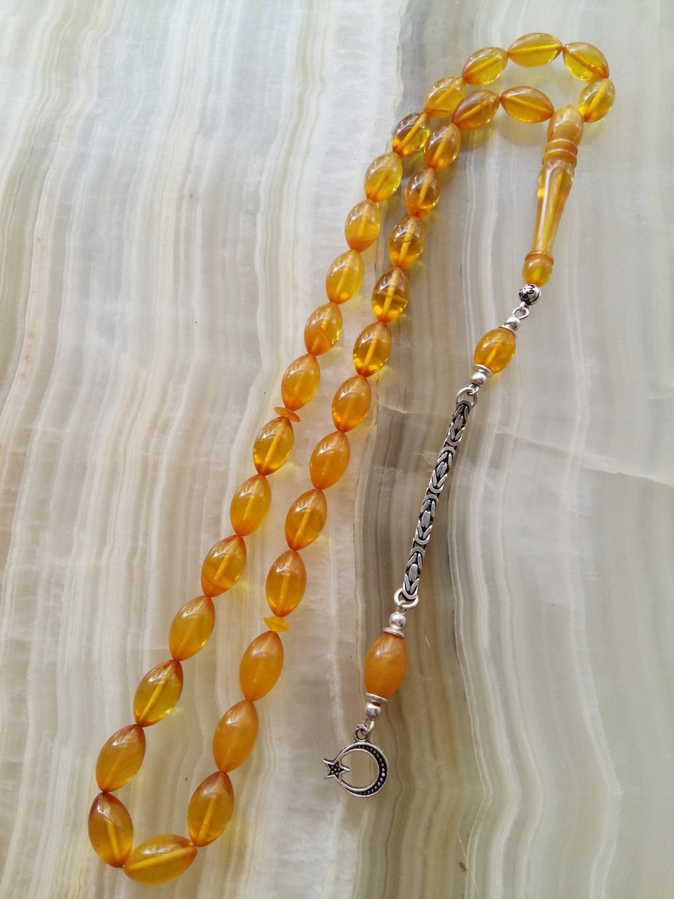 Özel İşçilikli Atölye Yapımı 925 Ayar Gümüş Püsküllü Sıkma Kehribar Tesbih.Ürün Piyasanın en iyi Hammaddesinden Yapılmış Olup Canlı Rengiyle, Yumuşak Dokusu ve Kusursuz İşçiligiyle Tesbih Severlerin Beğenisine Sunulmuştur.